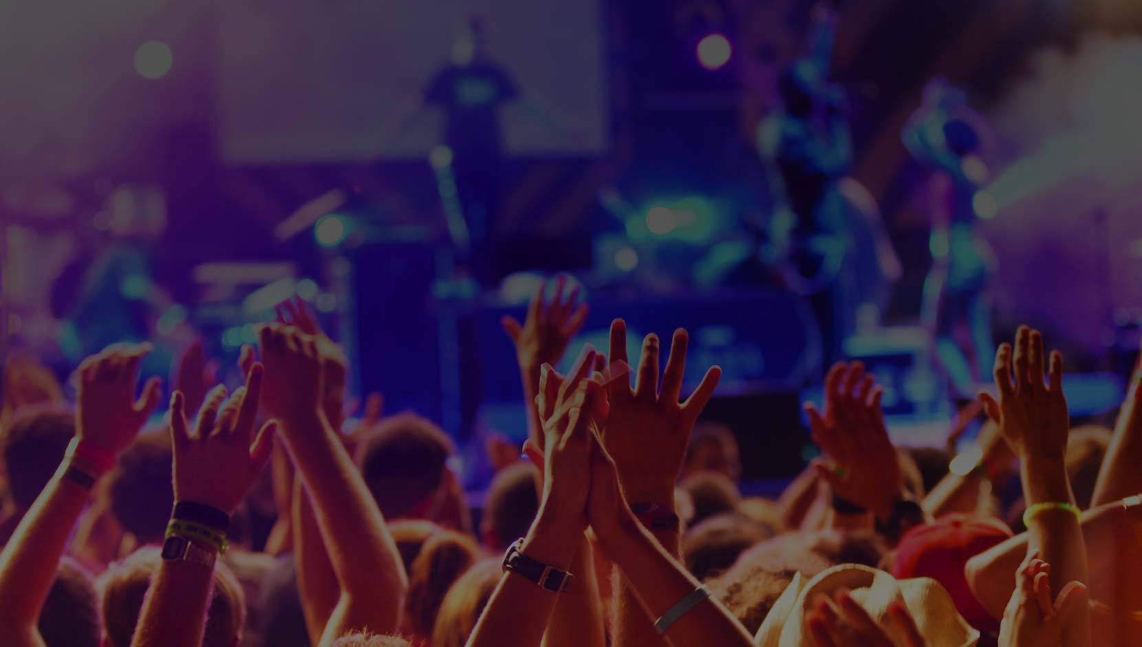 Concert crowd with hands raised in excitement.